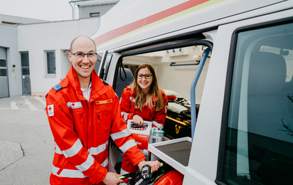 Zwei Sanitäter grinsen aus einem Rettungsauto